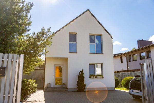 Nowoczesne domy z poddaszem otoczone zielenią i promieniami słońca.